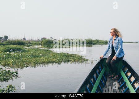 Young blonde woman in denim shirt ayant un tour de bateau le long des jardins flottants sur le lac Inle, Myanmar Banque D'Images
