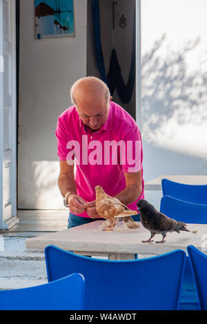 Mykonos, Grèce - 02 octobre 2011 : l'alimentation de l'homme locales pigeons dans une des ruelles, à Mykonos, l'île de Mykonos, Grèce Banque D'Images