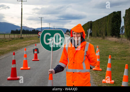 Une femme sur la route d'fonctionne un panneau routier et cônes de circulation dans un secteur dangereux sur une route de campagne, en Nouvelle-Zélande Banque D'Images