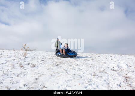 Boys sledding dans une pente avec le frère en attente en arrière-plan Banque D'Images