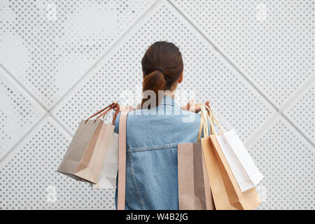 Vue arrière du jeune dame avec queue de cheval debout contre le mur carrelé et la tenue de tas de sacs de magasinage Banque D'Images