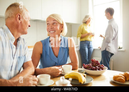 Portrait of happy young couple se regardant tendrement assis à table de cuisine à la lumière du soleil, copy space Banque D'Images