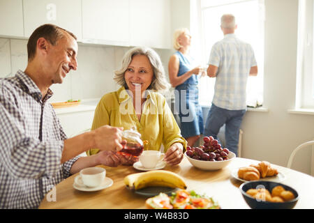Portrait of happy senior couple boire le thé dans une table de cuisine à la lumière du soleil, copy space Banque D'Images