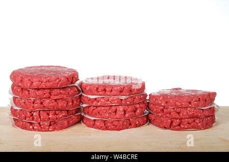 Des piles de galettes de viande hachée crue sur une table en bois avec des morceaux de papier sulfurisé entre les burgers pour les empêcher de coller. Isolé sur whi Banque D'Images