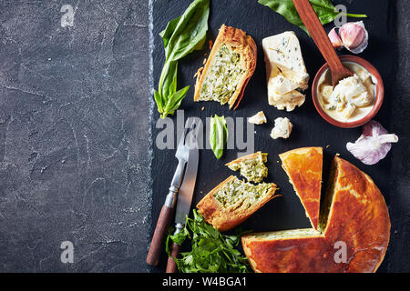 Close-up de haricots verts et épinards Tarte au fromage bleu ardoise noire en tranches sur un plateau avec crème au fromage bleu sauce dans un bol sur une table, la vue à partir de Banque D'Images