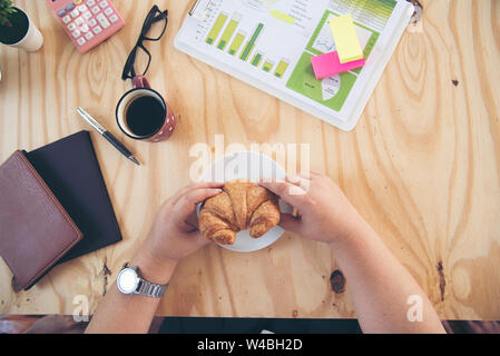 Chubby grosse femme ont un petit-déjeuner sur un bureau de travail. Croissant et café. Banque D'Images