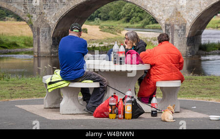 Les gens assis à un banc de pique-nique avec un certain nombre de bouteilles de boisson gazeuse, England, UK Banque D'Images