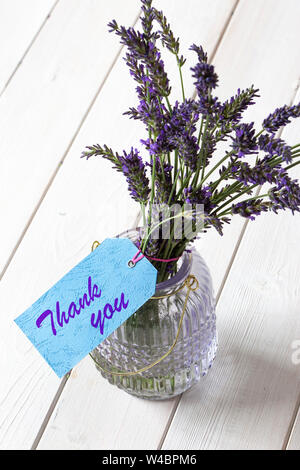 Bouquet de lavande dans un bocal de verre, avec merci écrit sur une étiquette cadeau bleu. Fond de bois blanc Banque D'Images