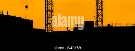 Arrière-plan de grue de construction silhouette de soulever des charges avec les rayons de soleil nuageux ciel du soir jaune toile de chantier à orange au coucher du soleil. Banque D'Images