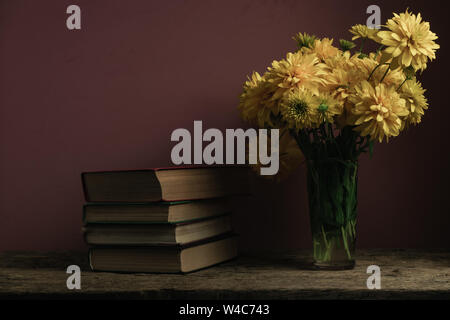 Livres anciens et de fleurs jaunes dans un vase sur une table en bois de chêne, dark-red wall background. Banque D'Images