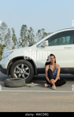 Woman waiting on road beside broken down car Banque D'Images