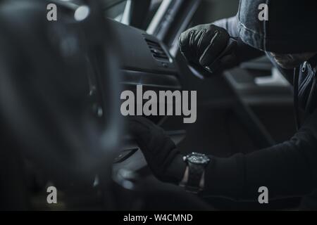 Voleur vêtu de noir à capuche à la recherche des objets de valeur à l'intérieur de la voiture. Pause en voiture par Thief Banque D'Images