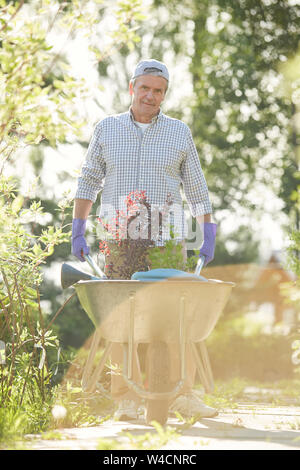 Portrait of mature man walking towards camera in sunlit jardin panier de plantes poussant Banque D'Images