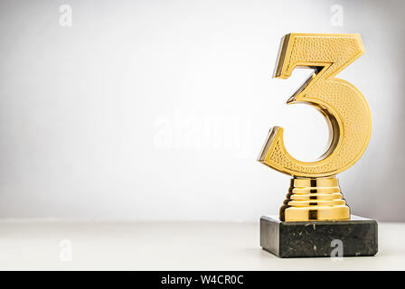 3ème placé runner up metallic gold trophy avec un numéro 3 en 3D sur un support placé sur le côté on white with copy space Banque D'Images