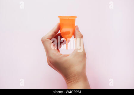 Woman's hand holding coupelle menstruelle sur fond rose. Banque D'Images