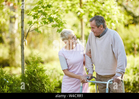 Taille portrait of senior man leaning on walker walking in park avec une infirmière ou femme, copy space Banque D'Images