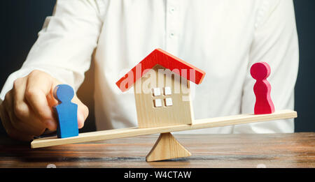 Figures en bois d'un homme et une femme sur les balances et une maison entre eux. La division des biens par des moyens légaux. La clarification de la propriété de l'immobilier Banque D'Images