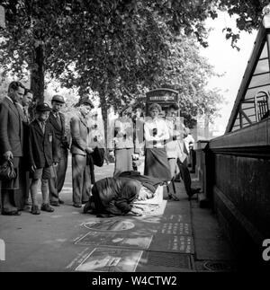 Une scène d'époque sur le remblai à Londres comme une foule se rassemble autour d'un artiste à l'œuvre de la chaussée avec sa craie dans les années 1950 Banque D'Images