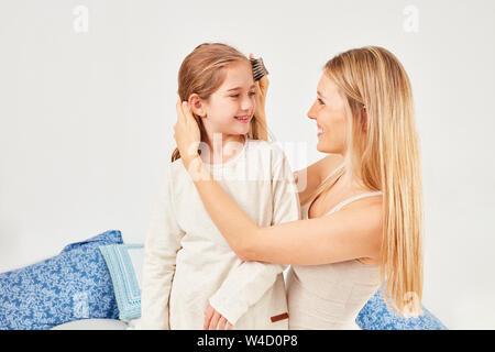 Mère attentive peignes les cheveux blonds de sa fille dans la chambre à coucher Banque D'Images