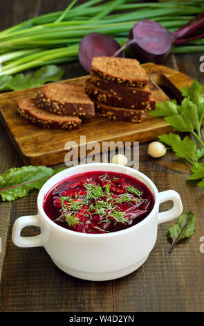 Soupe bortsch rouge avec de l'aneth dans un bol blanc sur la table en bois Banque D'Images