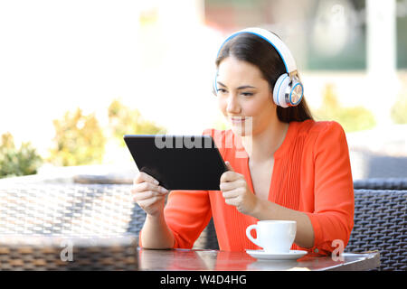 Femme concentré regarder et écouter des fichiers multimédia sur un tablet assis dans un bar terrasse Banque D'Images