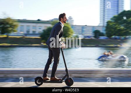 Jeune homme en costume d'équitation, un scooter électrique sur une réunion d'affaires. Banque D'Images