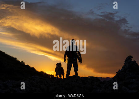 Le randonneur qui marche avec son chien au coucher du soleil dans la montagne Banque D'Images