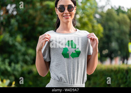 Young smiling attractive woman in Grey T-shirt avec symbole recyclage en parc. Banque D'Images