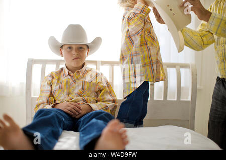 Portrait d'un garçon à ennuyer assis sur un lit à côté de son frère tout en portant un chapeau de cowboy. Banque D'Images