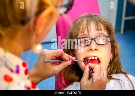 Portrait de petite fille douce avec la bouche ouverte, verres et insouciante expression sur son visage au cours de l'examen dentaire. Banque D'Images