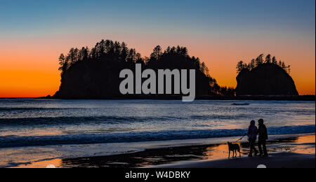 Un couple marche leur chien au coucher du soleil avec l'île James en arrière-plan. Banque D'Images