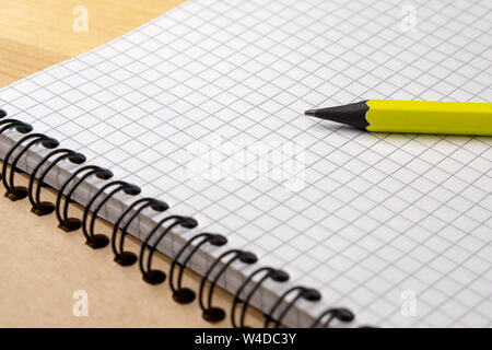 Crayon jaune sur un ordinateur portable avec des feuilles dans une cage sur une table en bois. Concept pour la liste d'achats, des notes, de la planification. Vue de côté. Banque D'Images