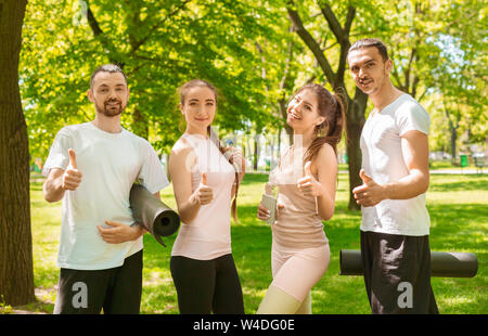 Quatre amis satisfait d'une formation réussie en plein air montrant Thumbs up Banque D'Images