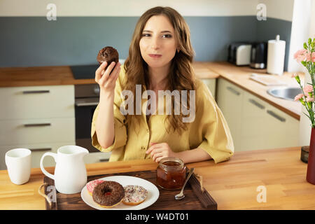 Belle jeune fille, c'est le petit-déjeuner à la maison dans la cuisine. Elle boit son café du matin et mange un muffin au chocolat. Banque D'Images