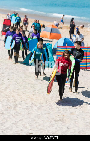 Un instructeur de surf de la plage de Fistral Surf School conduisant sa classe des apprenants à travers la plage de Fistral après une leçon de surf. Banque D'Images