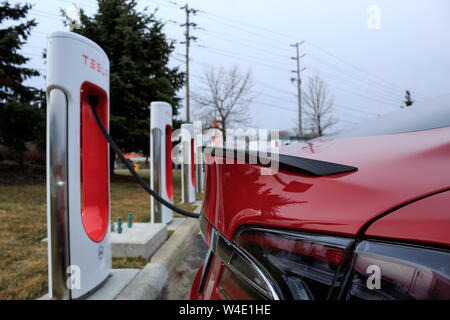 Tesla Model S rouge chez Tesla charge Supercharger comme vu avec fibre de carbone arrière Becquet. Banque D'Images