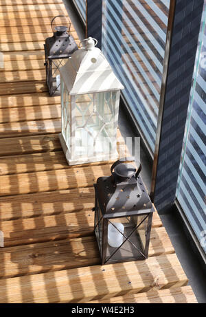 Lanternes blanc et brun sur un plancher en bois au cours d'une journée ensoleillée. Photographié en balcon avec verre rayé faisant belle clôture des ombres. Libre. Banque D'Images