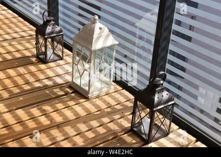 Lanternes blanc et brun sur un plancher en bois au cours d'une journée ensoleillée. Photographié en balcon avec verre rayé faisant belle clôture des ombres. Libre. Banque D'Images