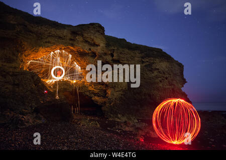 Deux amis de tourner une roue ardente de feu et un orbe rouge au cours d'une nuit d'aventure de la photographie de la plage et à proximité des grottes Banque D'Images