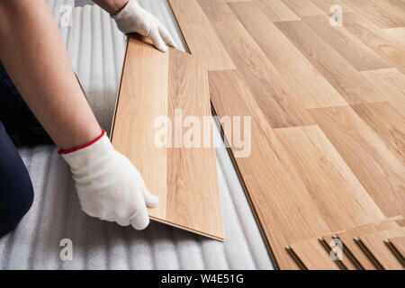 L'installation de plancher laminé, détail sur l'homme les mains avec des gants blancs en bois raccord tuile, plus de mousse blanche couche de base Banque D'Images