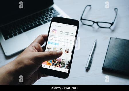 Nizhyn, Ukraine/ juillet-16-2019 : Jeune homme en appuyant sur écran à main page Instagram sur smartphone moderne. Ordinateur portable, lunettes, stylo et portable sur l'arrière-plan. Banque D'Images