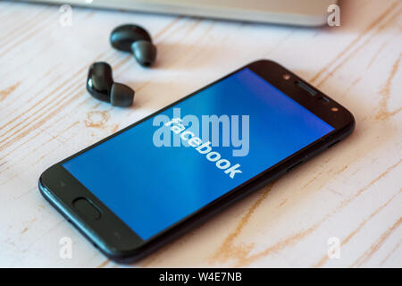 Nizhyn, Ukraine/Juillet-16-2019 : Smartphone avec application Facebook lancé et écouteurs écouteurs allongé sur la table. Social media concept. Banque D'Images
