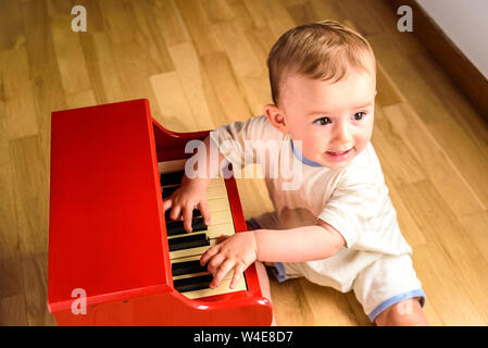 Bébé d'apprendre à jouer du piano avec un instrument, un jouet en bois tendre et drôle de scène de la petite enfance. Banque D'Images