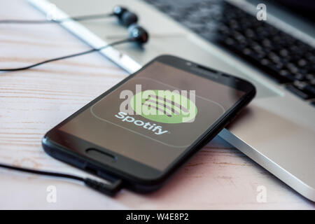 Nizhyn, Ukraine/Juillet-16-2019 : Smartphone avec Spotify app musique couché sur ordinateur portable avec des écouteurs Banque D'Images