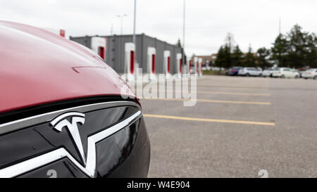 Tesla Model S rouge logo de calandre avant vu en-face de Tesla's FC Markham Supercharger emplacement. Banque D'Images