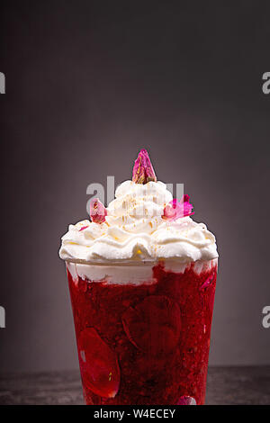 Fraise smoothie shake mélangé avec des pétales de rose et crème fouettée sur fond noir. Banque D'Images