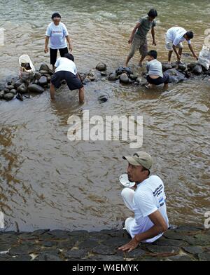 Bogor, Java ouest, Indonésie - Juillet 2019 : un groupe de personnes organiser des pierres pour construire un barrage dans la rivière Ciliwung, alors qu'un homme est assis sur le côté de la rivière. Banque D'Images