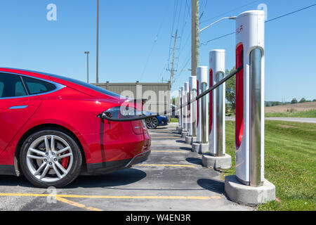 Tesla Model S rouge métallisé branché en charge, chez Tesla Supercharger. Banque D'Images