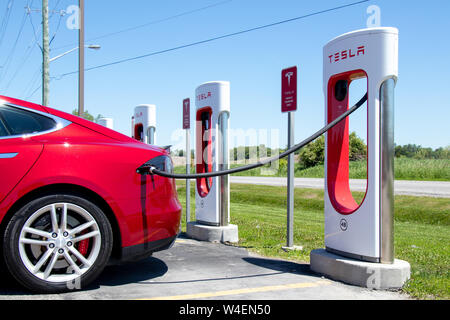 Tesla Model S rouge garée, recharge chez Tesla Supercharger. Banque D'Images