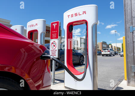 Tesla rouge branché en charge, chez Tesla Supercharger au King Crossing Fashion Outlet à Kingston, Ontario. Banque D'Images